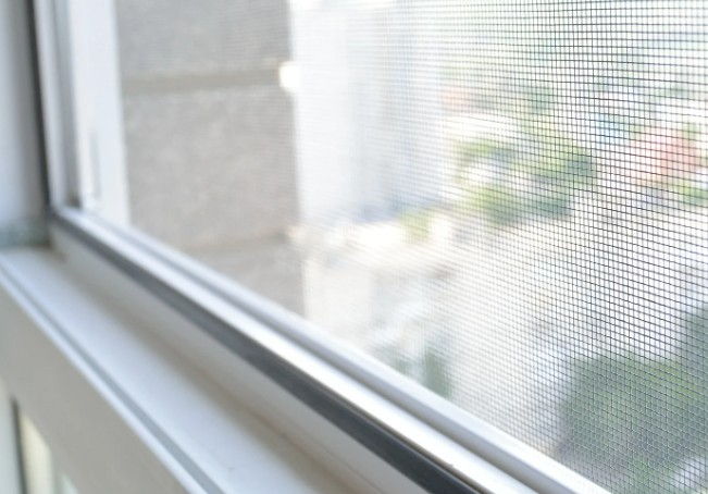 Malla de una mosquitera fija a medida montada en la ventana, vista desde el interior de la vivienda