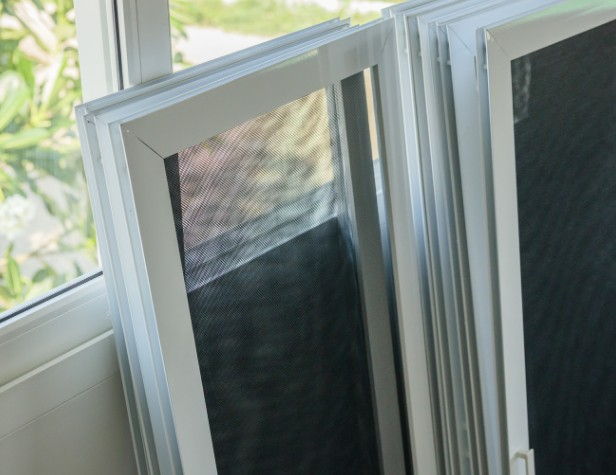 Mosquiteras con marco de aluminio blanco apiladas junto a una ventana, preparadas para su montaje en Burgos