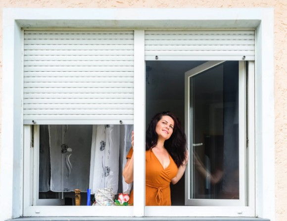 Mujer abriendo la ventana con la persiana de PVC blanca a media altura y el cajón exterior en un piso de bloque