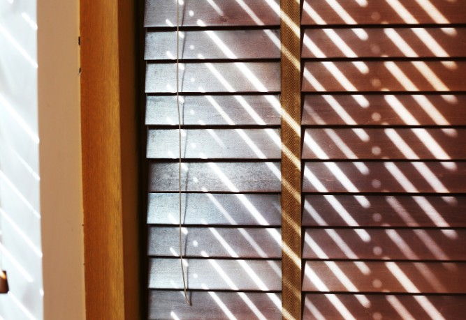 Veneciana de madera oscura filtrando la luz junto a la contraventana de un edificio antiguo